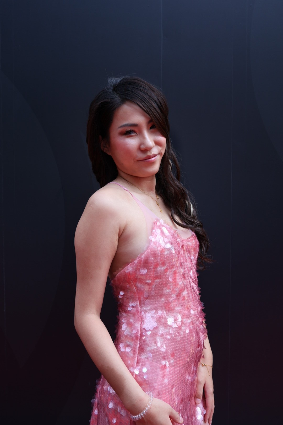 Enyu in a pink sequinned dress against a dark background
