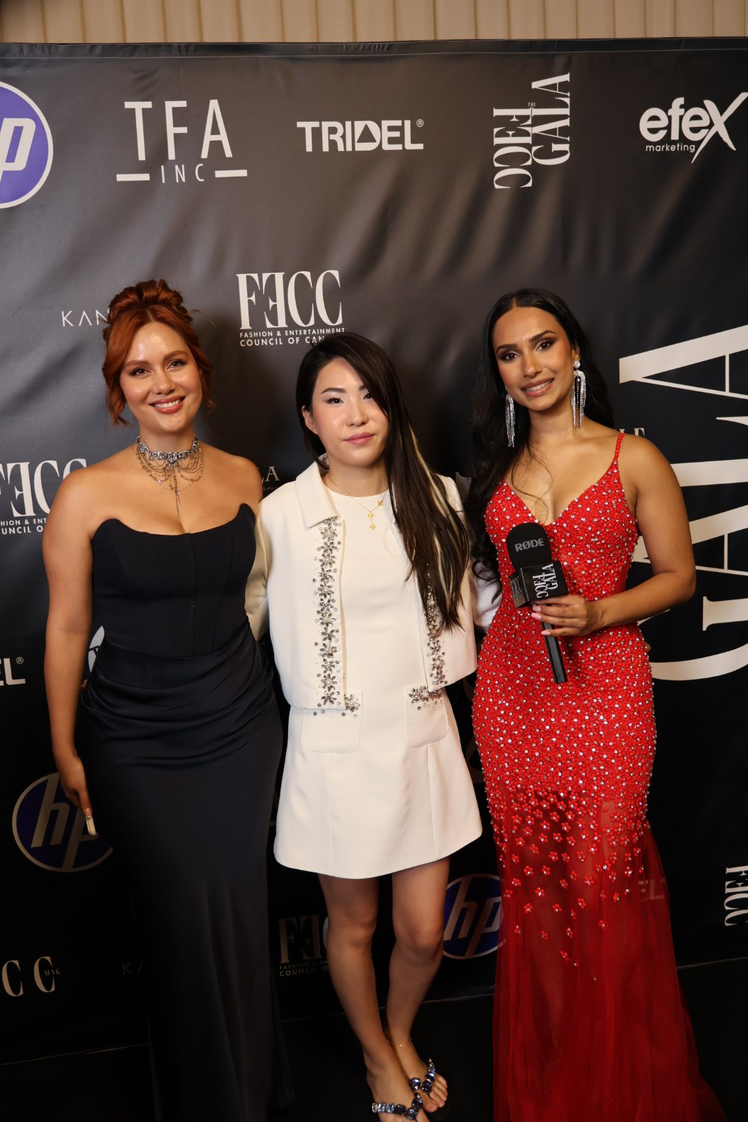 Enyu in a white embellished outfit with two guests at the FECC Gala backdrop