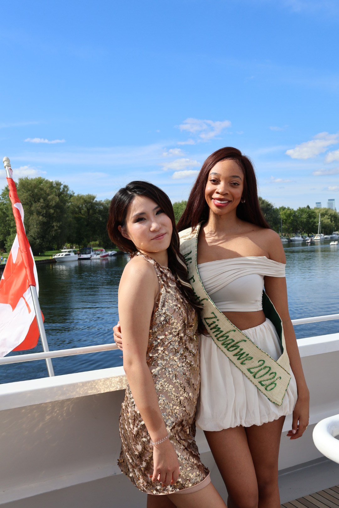 Enyu in a gold dress with a fellow guest on a sunlit boat deck